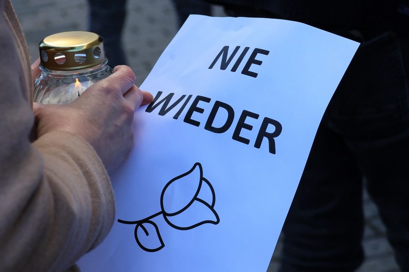 Jemand hält eine Kerze in der Hand und einen Zettel mit der Aufschrift "Nie wieder"